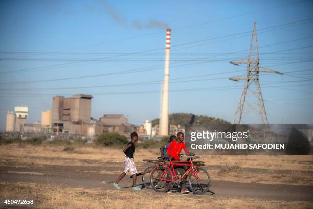 Children walk by a platinum mine as striking platinum miners gather at the Wonderkop Stadium in Marikana waiting to receive news on an ending strike...