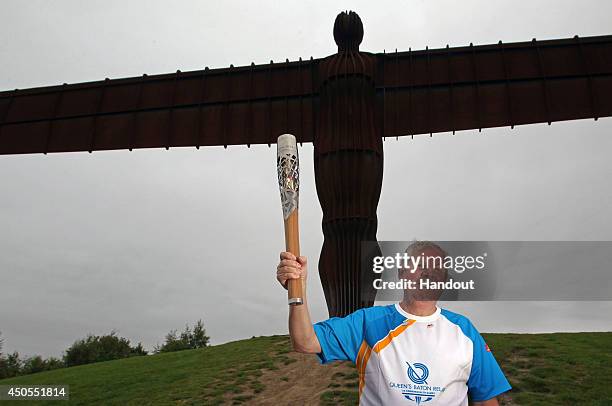 In this handout image provided by Glasgow 2014 Ltd, Baton bearers Brendan Foster holds the Queen's Baton in front of the Angel of the North on June...