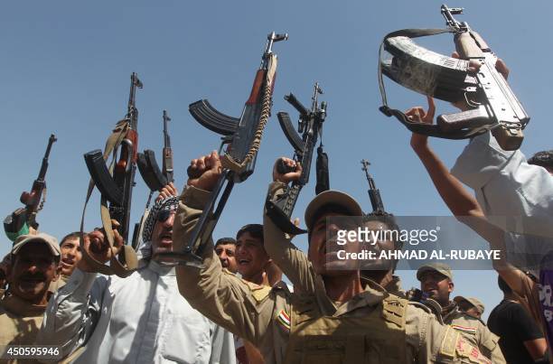 Iraqi Shiite men, some of them wearing military fatigues and guns given by the government, raise their weapons as they gather in the Iraqi town of...