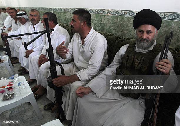 An Iraqi Shiite cleric holds his weapon as he sits at a recruitment centre in the Iraqi town of Jdaideh in the Diyala province on June 14 following...