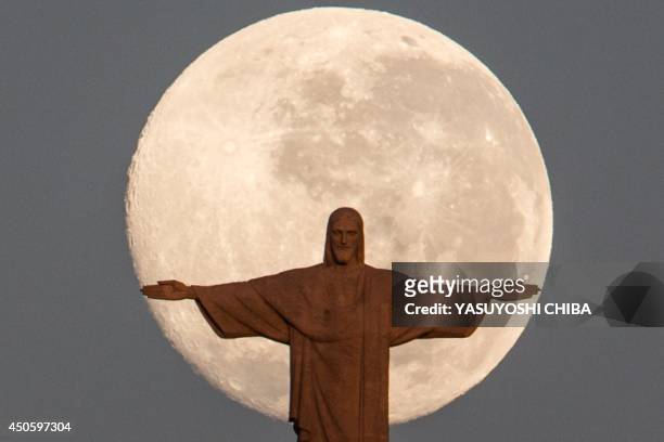 The moon sets behind the statue of Christ the Redeemer atop Corcovado hill in Rio de Janeiro, Brazil, on June 14, 2014. AFP PHOTO / YASUYOSHI CHIBA