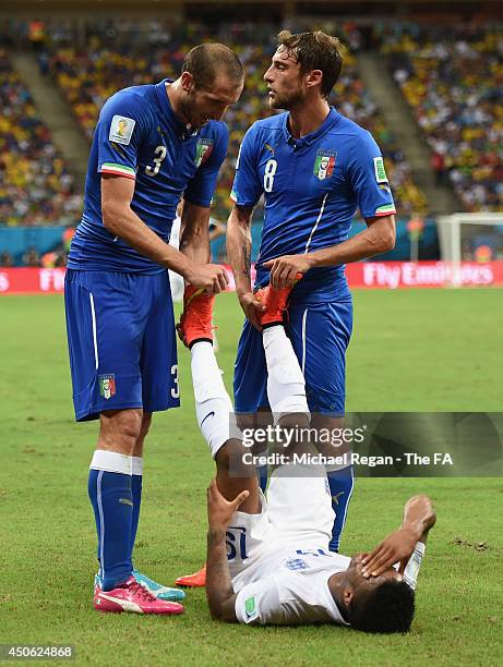 Giorgio Chiellini and Claudio Marchisio of Italy help Raheem Sterling of England stretch during the 2014 FIFA World Cup Brazil Group D match between...