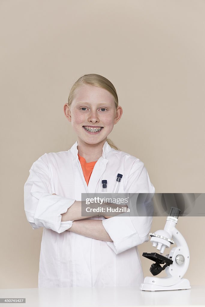 A smiling girl wearing a lab coat standing next to a microscope