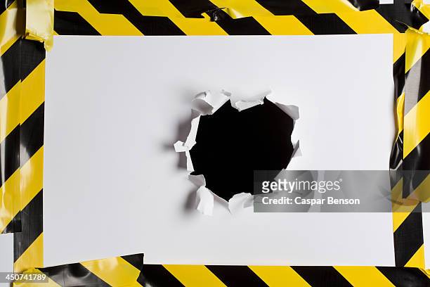 a punched out hole in cardboard with cordon tape around it - caution tape stock-fotos und bilder