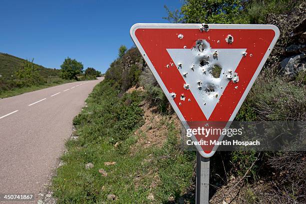 a yield sign with bullet holes in it posted on a remote highway - agujero de bala fotografías e imágenes de stock