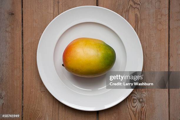mango on plate laying on wooden table - mangoes stock pictures, royalty-free photos & images