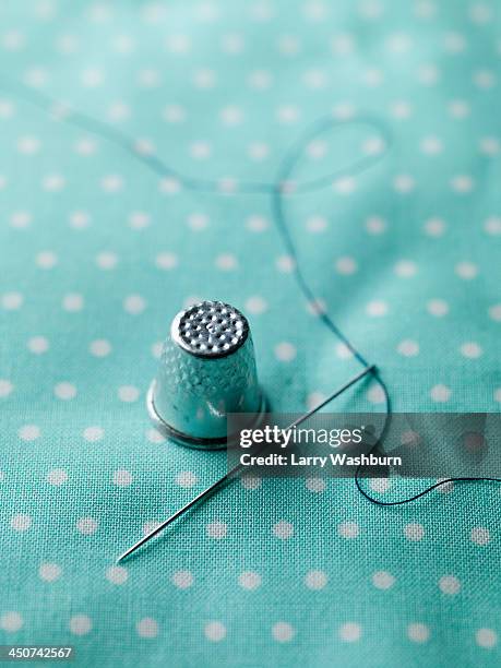 a threaded needle and thimble on top of polka dotted fabric - thimble fotografías e imágenes de stock