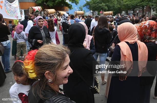 Bosnian woman, who has dyed part of her hair in the colors of the German flag for the World Cup, and other locals, including Muslim women, watch as a...