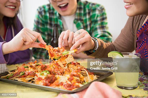 young women and man eating nachos with melted cheese - nachos stock pictures, royalty-free photos & images