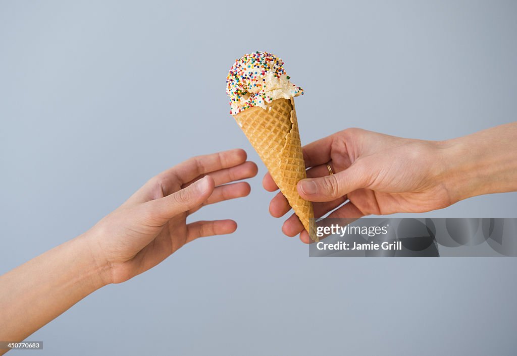 Hands passing ice cream against blue sky