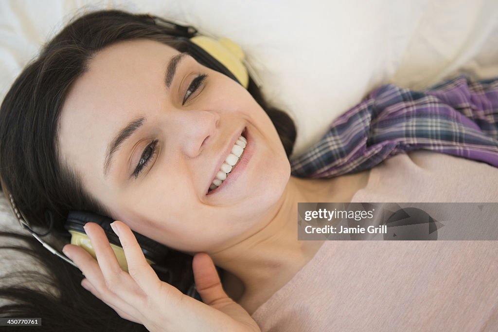Portrait of young woman lying down on bed and listening to music