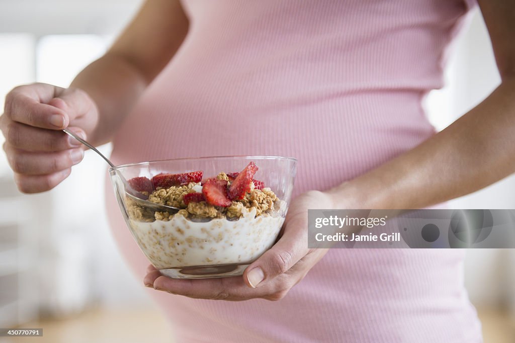 Mid section of pregnant woman holding bowl with granola