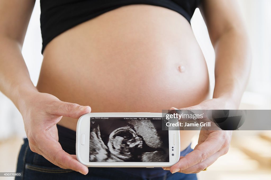 Mid section of pregnant woman holding mobile phone