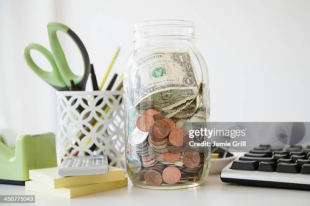 studio shot of jar full of money on desk - bureau de change stockfoto's en -beelden