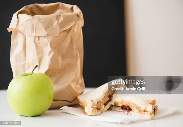 studio shot of green apple and sandwich next to paper bag - peanut butter and jelly sandwich stockfoto's en -beelden