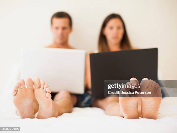 couple lying on bed with laptops - voetzool stockfoto's en -beelden