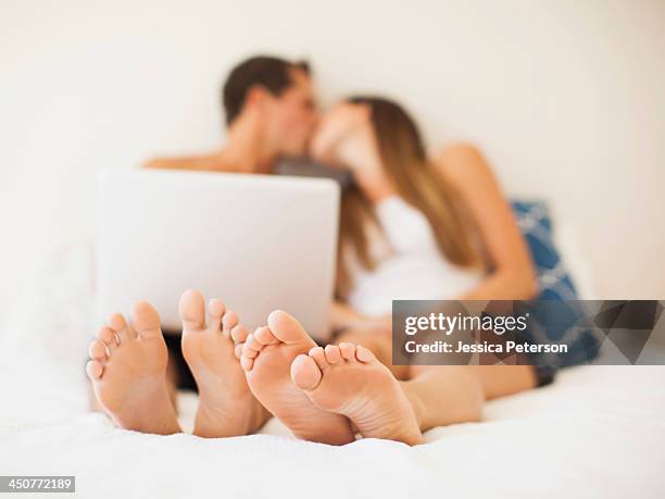 couple lying on bed with laptop - kissing feet stock pictures, royalty-free photos & images