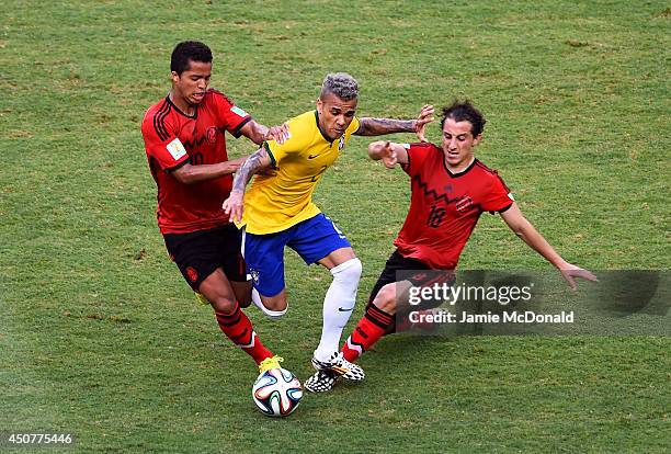 Dani Alves of Brazil is challenged by Giovani dos Santos and Andres Guardado of Mexico during the 2014 FIFA World Cup Brazil Group A match between...