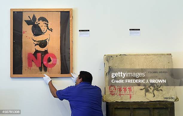 Ricardo Limon adjusts a display of streetartist Banky's work during a media preview for a coming auction at Julien's Auctions in Beverly Hills,...