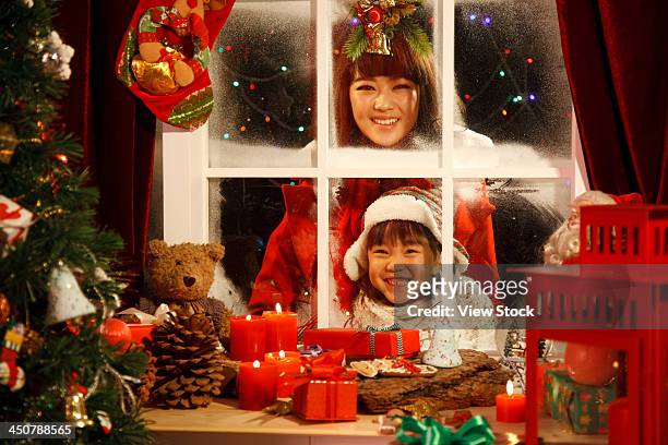 young woman and girl looking at christmas gift through window - woman looking through ice foto e immagini stock