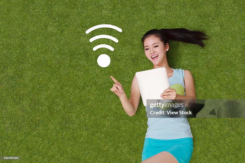 Young woman lying on grass with tablet