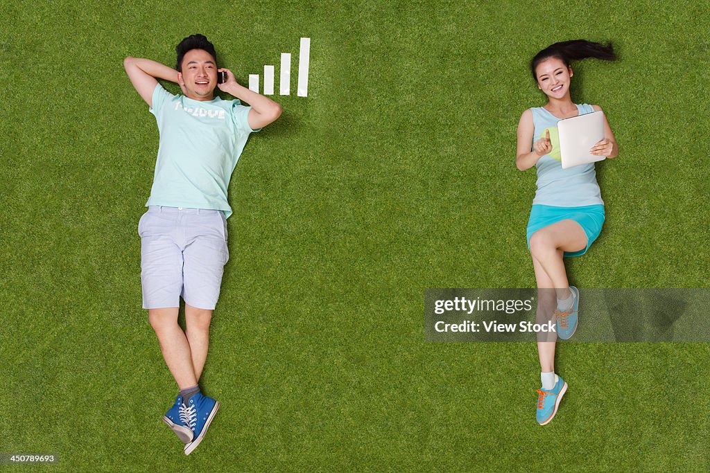 Young people lying on grass looking at phone and tablet