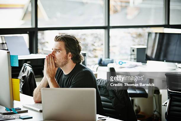 businessman with hands on chin at workstation - decisiones fotografías e imágenes de stock