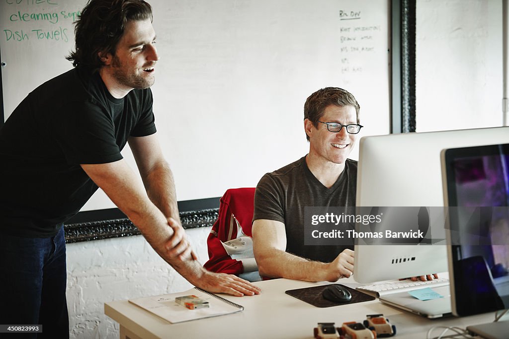 Smiling coworkers discussing project on computer