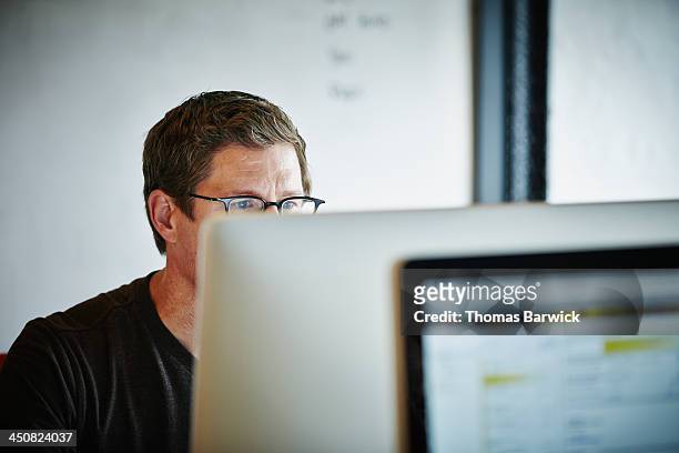 businessman sitting at desk working on computer - differential focus fotografías e imágenes de stock