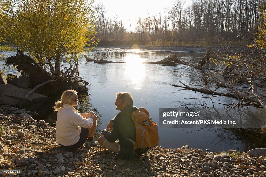 Couple relax beside river in autumn, conversing