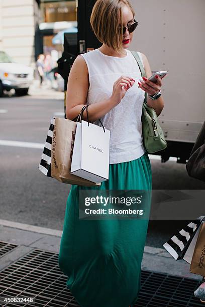 Woman carries a Chanel SA shopping bag while checking her mobile phone in the SoHo neighborhood of New York, U.S., on Wednesday, June 18, 2014. The...