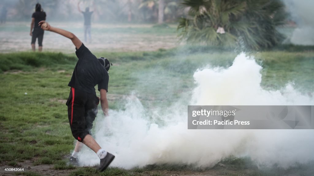 A masked man tries to throw back a canister of tear gas in a...