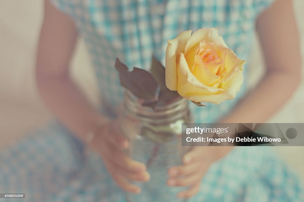 A young girl holding a yellow rose