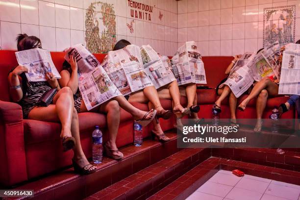 Indonesian commercial female sex workers cover their face as they sit behind the glass inside a brothel as it's activity still runs after being...