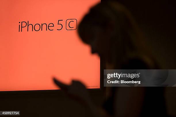 Visitor checks her smartphone in front of an iPhone 5c logo at Apple Inc.'s new Spanish flagship store on Puera de Sol square the day before opening...