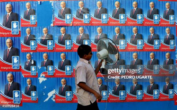 Maldivian man walks alongside a wall adorned with electoral posters of Maldives president and Dhivehi Rahyithunge Party's presidential candidate...