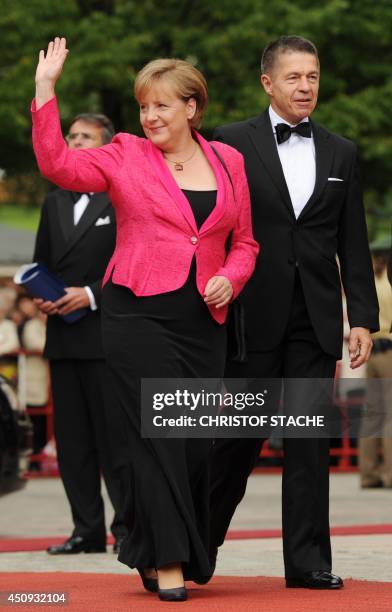 German Chancellor Angela Merkel waves as she arrives with her husband Joachim Sauer on the red carpet at the "Festspielhaus" ahead of the opening...