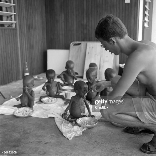 Refugee children, showing symptoms of Kwashiorkor malnutrition, receive food from a French military medical assistant, 15 March 1969, in the French...