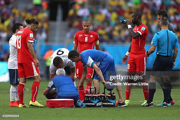 Steve von Bergen of Switzerland receives treatment as teammate Gokhan Inler and Olivier Giroud of France look on during the 2014 FIFA World Cup...