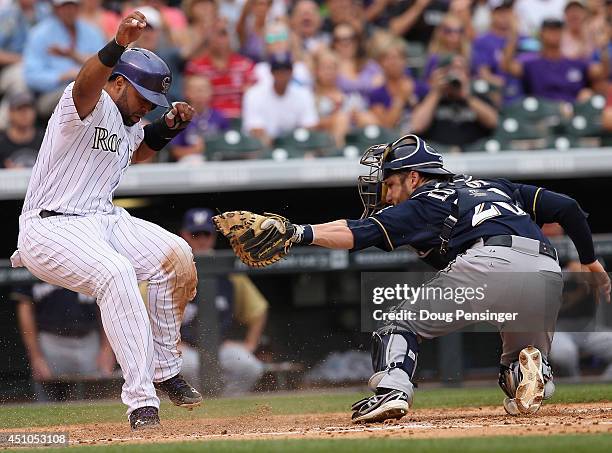 Wilin Rosario of the Colorado Rockies slides around catcher Jonathan Lucroy of the Milwaukee Brewers to score on a single by Charlie Blackmon of the...