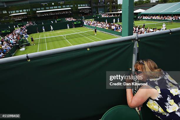 Fan peaks through a gap in the fence to watch the tennis action on day one of the Wimbledon Lawn Tennis Championships at the All England Lawn Tennis...