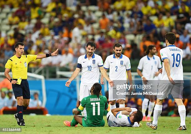 Referee Carlos Vera shows a yellow card as Didier Drogba of the Ivory Coast and Giorgos Karagounis of Greece talk after a collision between Drogba...