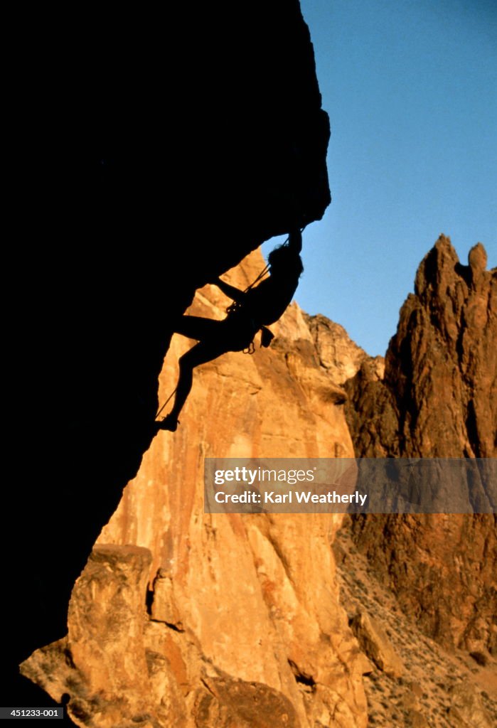 Rock climber climbing up rock overhang, silhouette