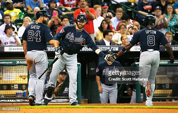 Ryan Doumit of the Atlanta Braves greets Evan Gattis and Justin Upton after Upton hit a sacrifice fly to score Gattis in the second inning of their...