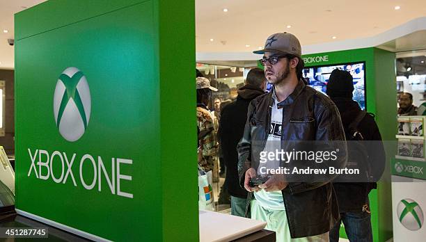 Man plays an XBox One - a new video game console and home entertainment system made by Microsoft- while waiting in line to buy an XBox One from a...