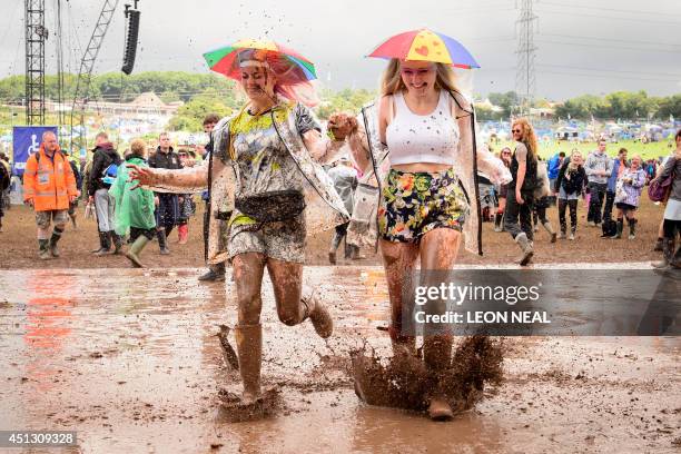 Revellers run through a puddle as they pose for photographers, on the first official day of the Glastonbury Festival of Music and Performing Arts on...