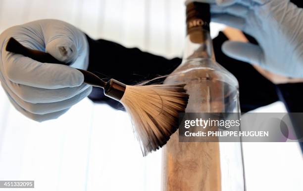 Member of the forensic section of the French gendarmerie brushes a bottle to take fingerprints at a police station in Beauvais on November 21, 2013....