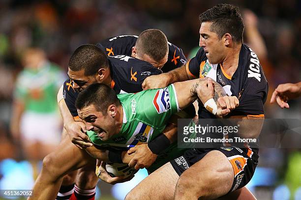 Paul Vaughan of the Raiders is tackled by is tackled by the Tigers defence during the round 16 NRL match between the Wests Tigers and the Canberra...