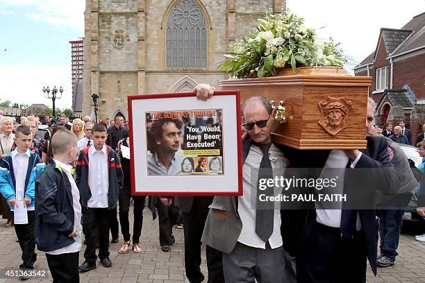 Mourner holds a framed newspaper headline as he carries the coffin of Gerry Conlon, from St Peters Cathedral in west Belfast on June 28, 2014....
