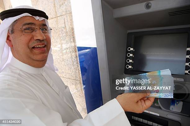 Kuwaiti man holds up the the sixth edition of a 20 Kuwaiti Dinar bill, that was recently put into circulation by the Central Bank, next to an ATM in...